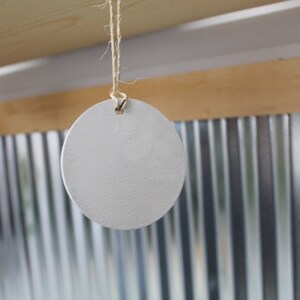 May include: A white, round, wooden tag hangs from a string. The tag is blank and ready to be labeled.