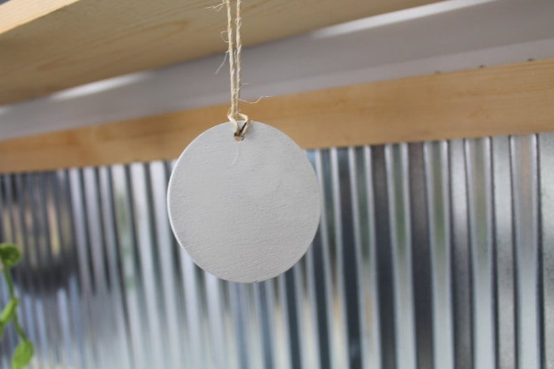 May include: A white, round, wooden tag hangs from a string. The tag is blank and ready to be labeled.