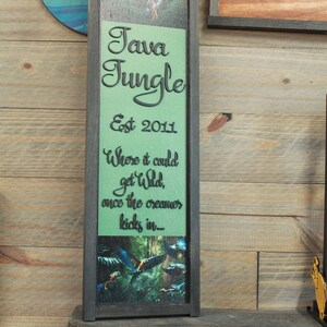 May include: A framed wooden sign with the text "Java Jungle Est 2011" in black script on a green background. The sign also includes the phrase "Where it could get Wild, once the creamer kicks in..." and a picture of parrots.