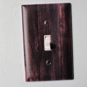 May include: A light switch cover with a wood grain pattern in shades of brown and purple. The switch is white and says "ON" and "OFF".