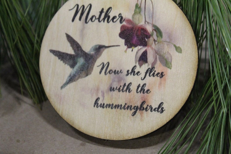 May include: A wooden ornament with a hummingbird and a flower, and the text "Mother Now she flies with the hummingbirds".