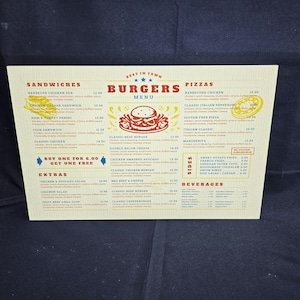 May include: A printed menu featuring sandwiches, burgers, pizzas, sides, and beverages. The menu has a vintage design with a red and yellow color scheme. The word "Burgers" is prominently displayed at the top.