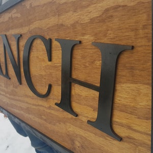 May include: A wooden sign with black raised letters spelling "KRANCH" on a brown wood background with a black frame.