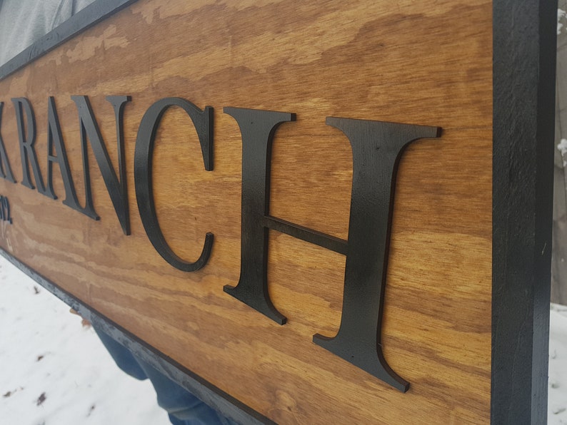 May include: A wooden sign with black raised letters spelling "KRANCH" on a brown wood background with a black frame.