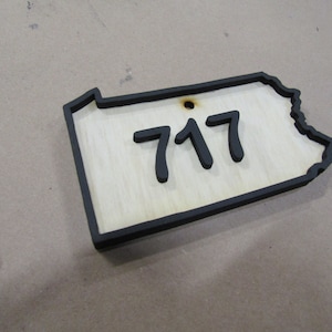 May include: A wooden cutout of the state of Pennsylvania with a black border and the number 717 inside.