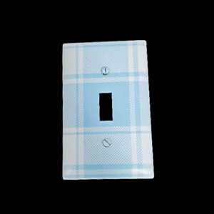 May include: A decorative light switch cover with a blue and white plaid pattern. The cover has a rectangular shape with a single switch opening and two screw holes. The design features a light blue square in the center.