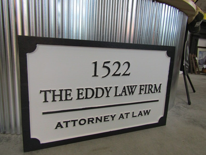 Puede incluir: Un letrero blanco con letras negras y un borde negro. El letrero dice "1522 The Eddy Law Firm Attorney at Law".