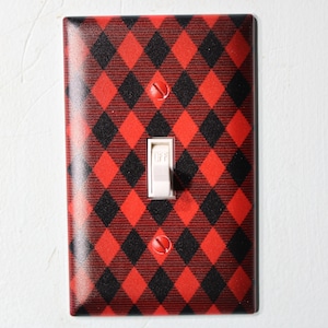 May include: A light switch cover with a red and black buffalo plaid pattern. The switch is in the off position.