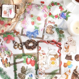 May include: A collection of colorful stickers featuring illustrations of animals, food, and nature. The stickers are on a white background and include a donut, a butterfly, a bunny, a bear, a strawberry, a pine cone, and a blue bow.