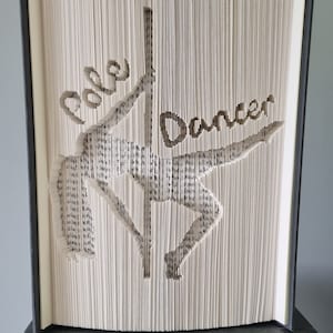 May include: A book with the words "Pole Dancer" cut out of the pages, creating a silhouette of a person pole dancing.