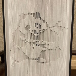 May include: A white paper book with a 3D pop-up design of a cartoon character. The character is a white bear wearing a black hat and a black scarf. The bear is sitting on a white background.