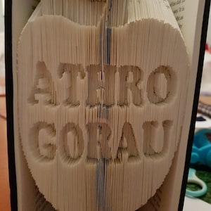 May include: A white book folded into the shape of an apple with the words "ATHRO GORAU" in the center.