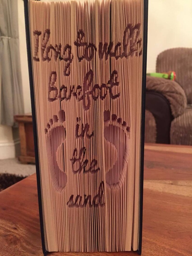 May include: A book with the words "Long to walk barefoot in the sand" folded into the pages. The words are cut out of the pages and the book is standing upright.