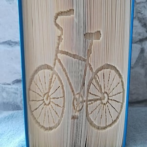 May include: A book with the pages folded to create a 3D sculpture of a bicycle. The sculpture is made from the pages of a book, and the bicycle is in a light brown colour.