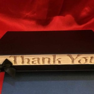 May include: A black book with a white spine that says "Thank You" in a decorative font. The book has a black ribbon bookmark.