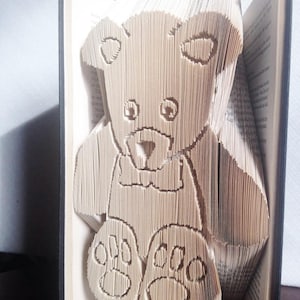 May include: A brown teddy bear made from folded pages of a book. The bear is sitting upright with its paws in front of it.