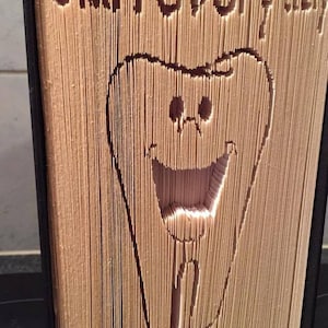 May include: A book with a folded paper design of a smiling tooth. The text "Start every day with a smile" is cut into the pages.