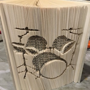 Peut inclure: Un livre dont les pages sont pliées en un motif tridimensionnel d'un oiseau en vol. Le livre est fait de papier blanc et a une couverture brune.
