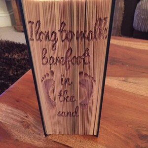 May include: A book with the text "I long to walk barefoot in the sand" carved into the pages. The book is folded into a three-dimensional sculpture.