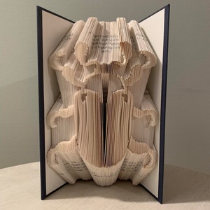 Puede incluir: Una escultura de arte de libro de un escarabajo, hecha doblando las páginas de un libro. El libro está encuadernado en azul marino y la escultura está de pie sobre una superficie de madera clara.