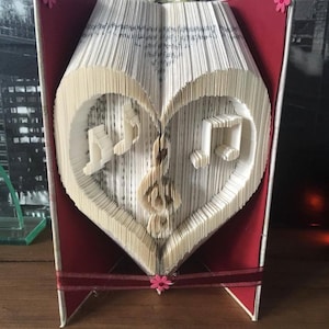 May include: A red book with a heart-shaped book fold-out, decorated with musical notes. The book is standing on a wooden surface.