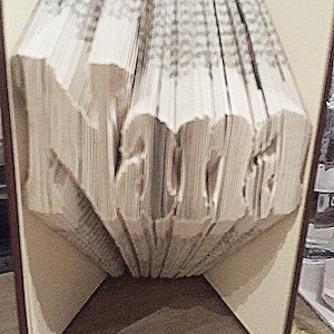May include: A book folded into the shape of the word "LOVE" with the pages fanned out. The book is standing upright on a wooden surface.