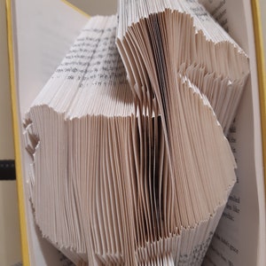 May include: A book folded into a three-dimensional shape, creating a unique and intricate design. The pages are folded in a way that creates a series of peaks and valleys, giving the book a textured appearance.