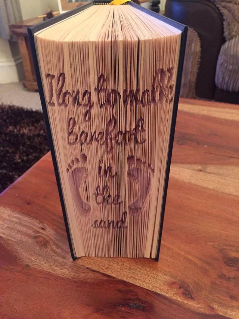 May include: A book with the words "I long to walk barefoot in the sand" cut out of the pages. The book is folded into a three-dimensional shape.