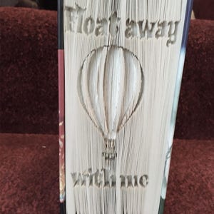 May include: A book with the pages folded to create a 3D sculpture of a hot air balloon. The text "Float away with me" is cut into the pages.