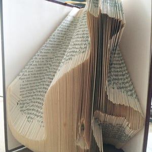 May include: A book folded into the shape of a cat. The pages are folded in a way that creates a three-dimensional effect. The book is open and the pages are visible.