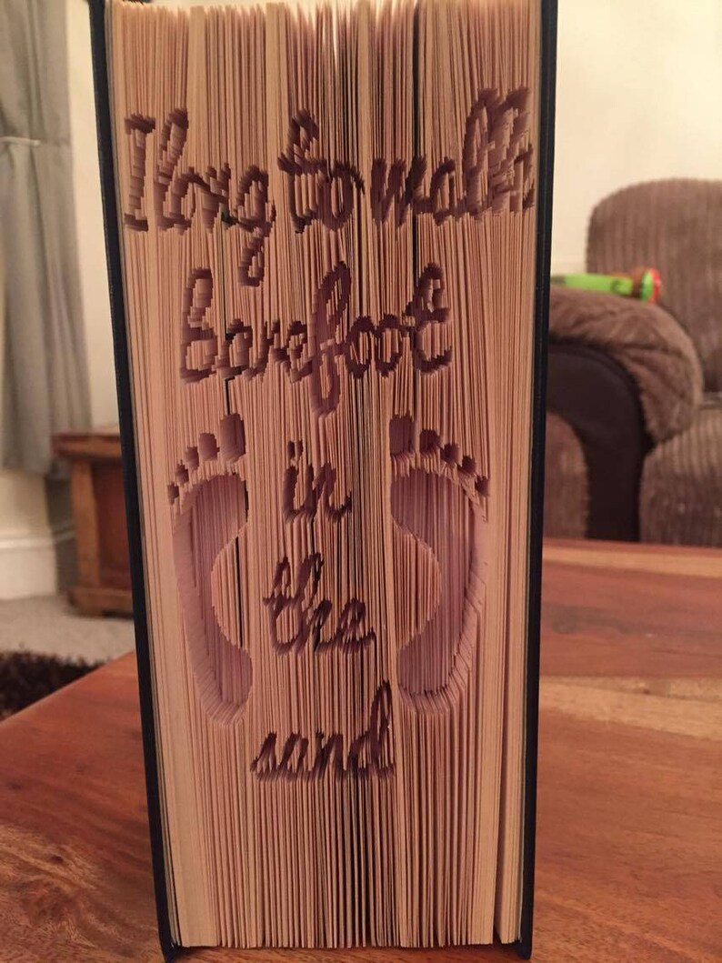May include: A book with the words "Long to walk barefoot in the sand" cut out of the pages. The book is standing upright on a wooden surface.