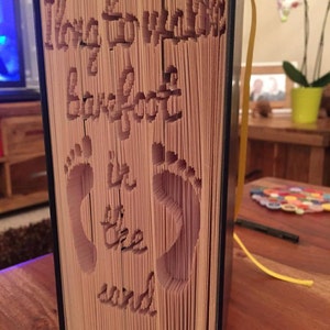 May include: A book with the words "Love to walk barefoot in the world" cut out of the pages. The pages are folded to create a 3D effect.