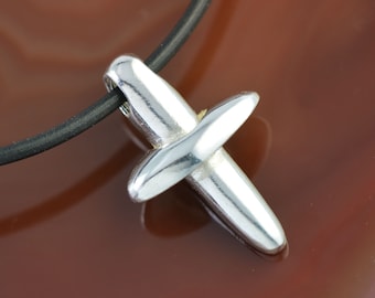 May include: A silver cross pendant on a black leather cord necklace. The cross has a simple, modern design.