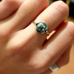Puede incluir: Un anillo de plata con un dise&ntilde;o redondo en forma de moneda que presenta el perfil de la cara de una mujer.