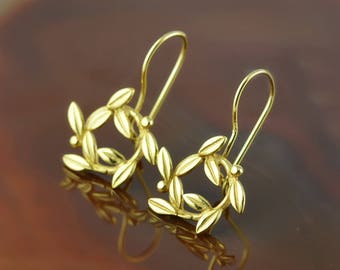 Puede incluir: Un par de pendientes de oro con un delicado diseño de rama de olivo. Los pendientes están hechos de un metal liso y brillante y tienen un estilo simple y elegante.