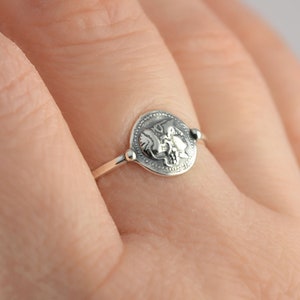 Puede incluir: Un anillo de plata con un dise&ntilde;o redondo y detallado que presenta dos p&aacute;jaros enfrentados. El anillo se lleva en un dedo.