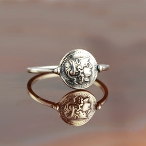 Puede incluir: Un anillo de plata con un dise&ntilde;o redondo en forma de moneda que presenta el perfil de la cara de una mujer. El anillo es simple y elegante.
