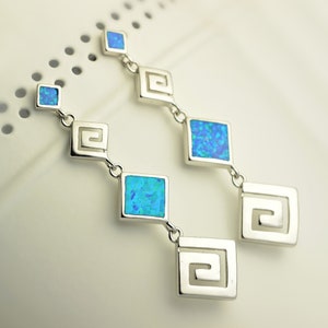 May include: A pair of silver earrings with blue opal stones and a geometric design. Each earring has three square-shaped stones and a square-shaped design with a Greek key pattern.
