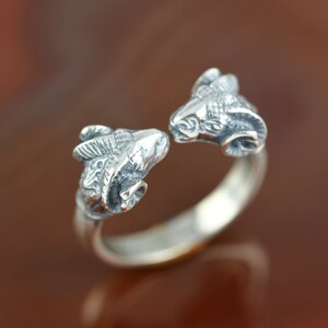 May include: A silver ring with two ram heads facing each other. The ring is open and the ram heads are detailed.
