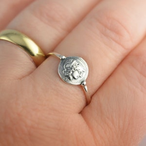 Puede incluir: Un anillo de plata con un dise&ntilde;o redondo y detallado que presenta una criatura m&iacute;tica. El anillo se lleva en un dedo.