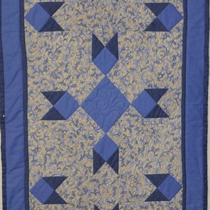 May include: A blue and beige quilted table runner with a geometric pattern. The runner features a repeating design of blue stars on a beige background.
