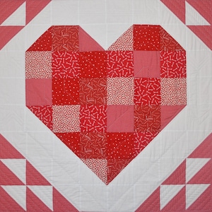 May include: A red and white patchwork quilt with a large heart shape in the center. The heart is made up of smaller squares of fabric with different patterns, including hearts, keys, and polka dots. The quilt is surrounded by a white border with red and white triangles.