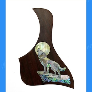 May include: Rosewood Taylor pickguard with a howling wolf design. The pickguard is dark brown with an inlaid wolf illustration, a full moon, and iridescent accents. The text reads "Rosewood Taylor Pickguard fit 5.5" Rosette".
