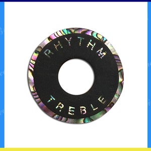 Puede incluir: Placa de interruptor de palanca de ébano con un centro negro y un borde decorativo de nácar. La placa tiene las palabras "Rhythm" y "Treble" inscritas en ella.