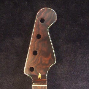 May include: Close-up of a 4-string electric bass neck. The headstock is a dark brown with a wood grain pattern, four circular holes, and a decorative edge. The text "Bruce Wei 4 String Electric Bass Neck GN-2104" is at the bottom.