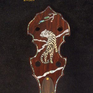 Puede incluir: Mástil de banjo de 5 cuerdas hecho a mano con incrustaciones de tigre. El clavijero es de color marrón oscuro con detalles de concha de abulón y un diseño de tigre blanco. El texto "Bruce Wei Handmade 5 String Banjo Neck BN-2019" está en la parte superior.