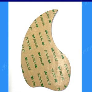 May include: A brown acoustic guitar pickguard with a rounded shape and adhesive backing. The pickguard is covered in 3M 300LSE adhesive tape.