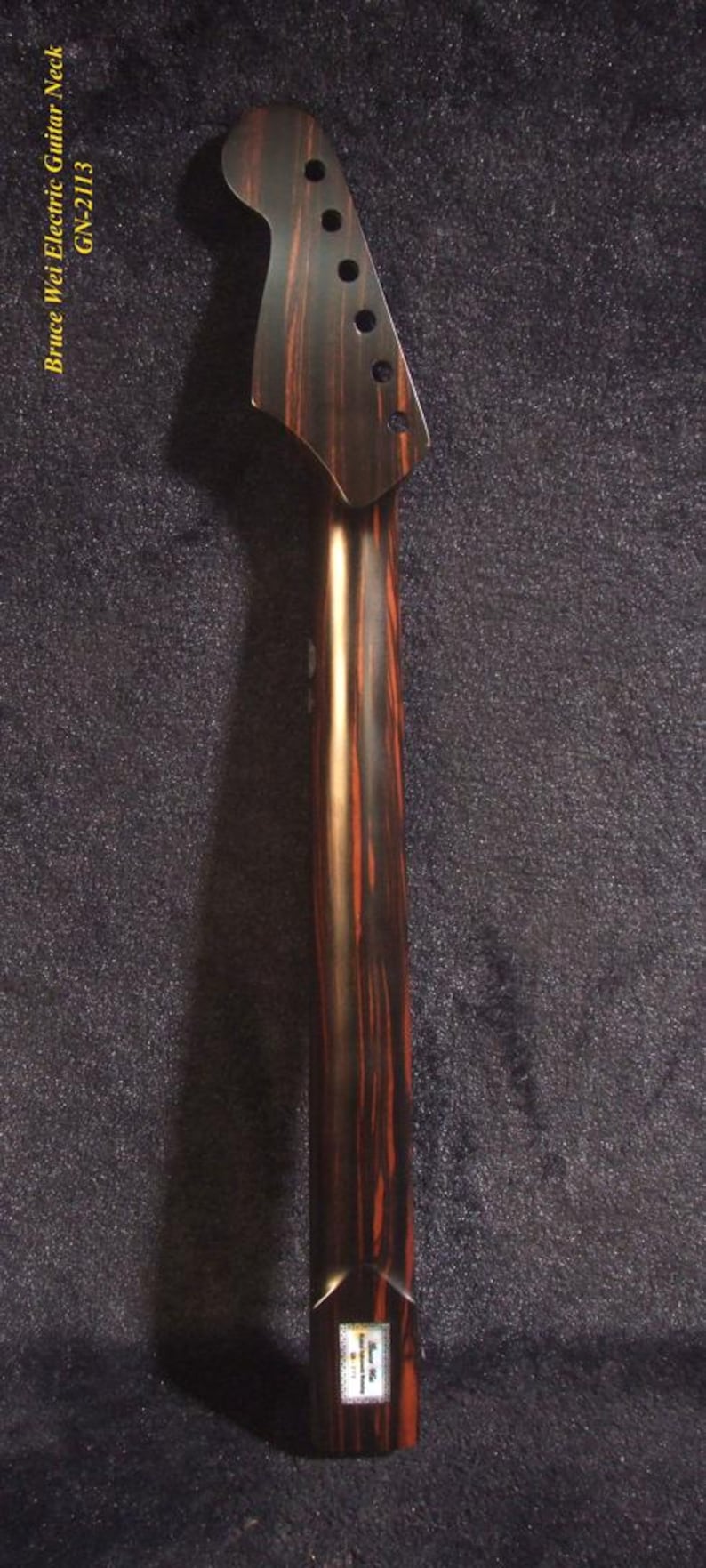 May include: A guitar neck with a dark brown and reddish-brown wood grain pattern. The headstock has six tuning peg holes. The text "Bruce Wei Electric Guitar Neck GN-2113" is visible.