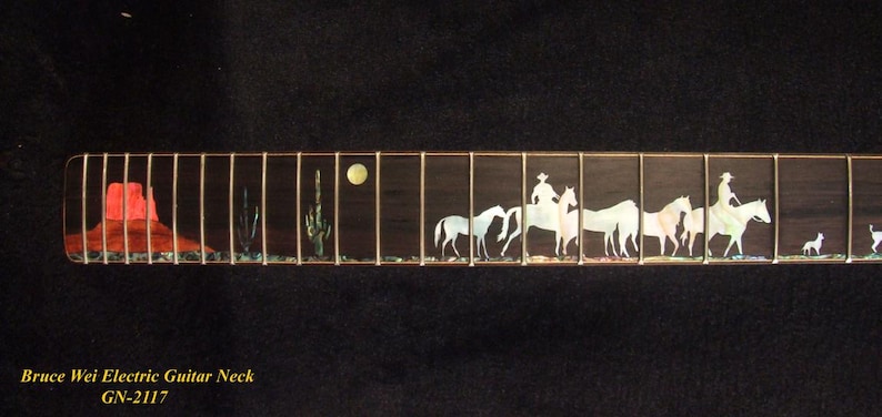 May include: A guitar neck with a desert scene inlay. The inlay features a red rock formation, cacti, a full moon, cowboys on horseback, and a dog. The fretboard is dark brown with gold frets.