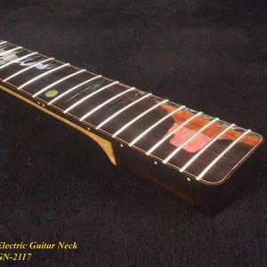 May include: Close-up of an electric guitar neck with white frets on a dark wood fretboard. The neck has a natural wood finish and a decorative inlay. The text "Bruce Wei Electric Guitar Neck GN-2117" is visible.
